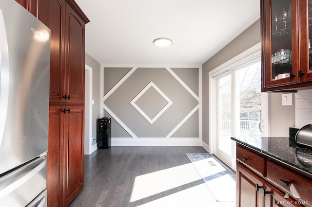 kitchen featuring dark stone countertops, freestanding refrigerator, glass insert cabinets, baseboards, and dark wood-style flooring