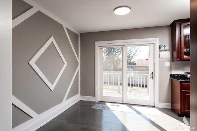 doorway with dark wood-type flooring, visible vents, and baseboards