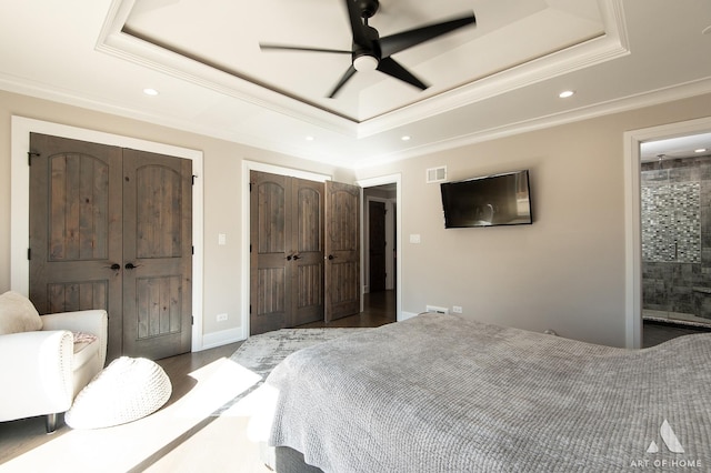 bedroom with wood finished floors, visible vents, a tray ceiling, ornamental molding, and multiple closets