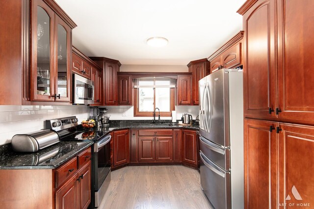 kitchen featuring a sink, dark stone countertops, appliances with stainless steel finishes, light wood finished floors, and glass insert cabinets