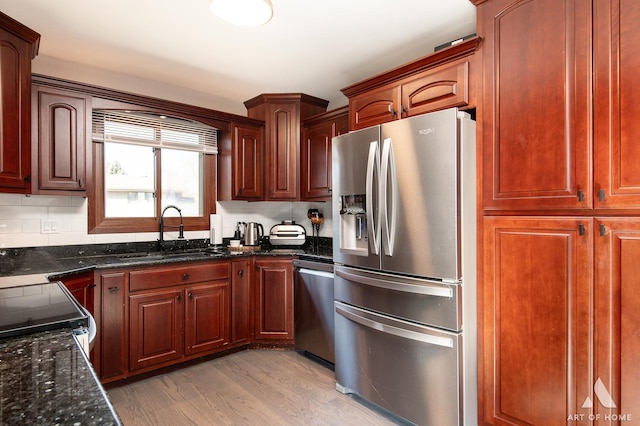 kitchen featuring dark stone countertops, a sink, decorative backsplash, light wood-style floors, and appliances with stainless steel finishes