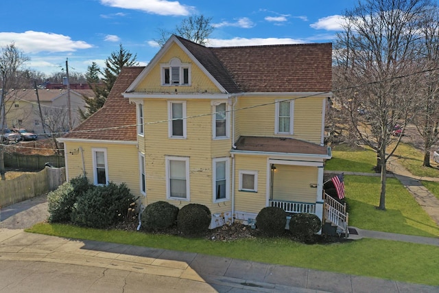 view of front of house with fence, a porch, a front lawn, and a shingled roof