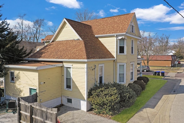 view of home's exterior featuring fence and a shingled roof