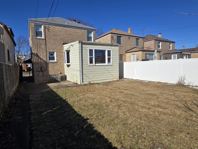 back of house featuring a yard, brick siding, a patio, and a fenced backyard