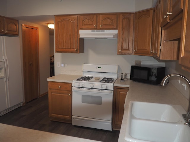 kitchen with dark wood finished floors, light countertops, a sink, white appliances, and under cabinet range hood