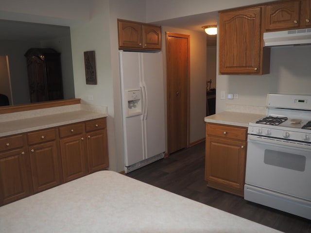 kitchen with under cabinet range hood, white appliances, light countertops, brown cabinets, and dark wood-style floors