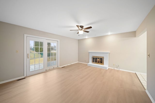 unfurnished living room with ceiling fan, visible vents, baseboards, a brick fireplace, and light wood finished floors