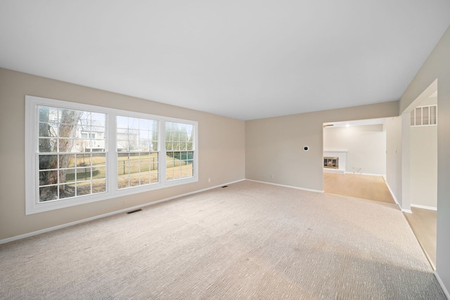 spare room featuring light carpet, a lit fireplace, visible vents, and baseboards