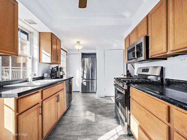 kitchen featuring stainless steel appliances, dark countertops, a sink, and a ceiling fan