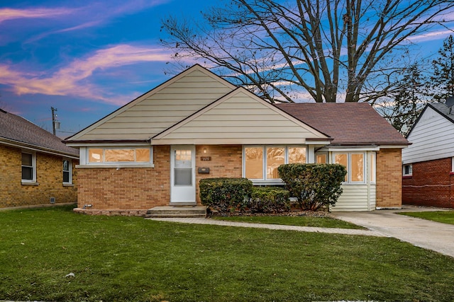 view of front facade with entry steps, brick siding, a front yard, and a shingled roof