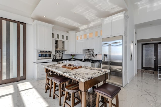 kitchen featuring decorative backsplash, wall chimney range hood, marble finish floor, and stainless steel appliances