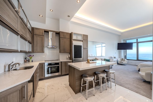 kitchen featuring oven, wall chimney range hood, a kitchen bar, a tray ceiling, and a sink