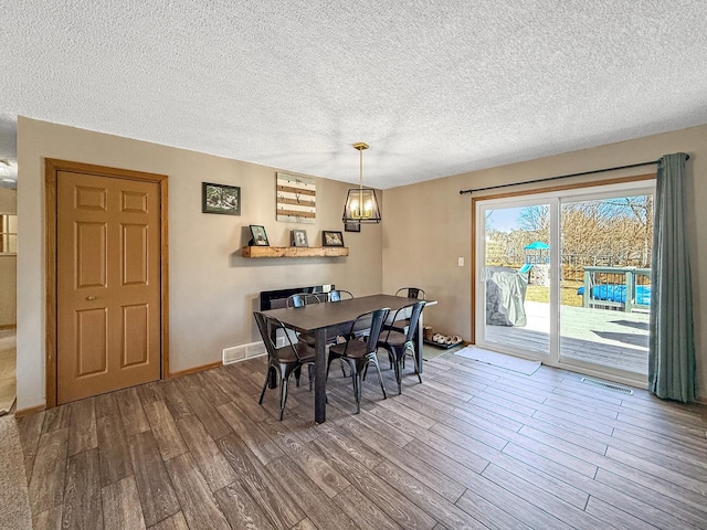 dining area with a textured ceiling, wood finished floors, visible vents, and baseboards