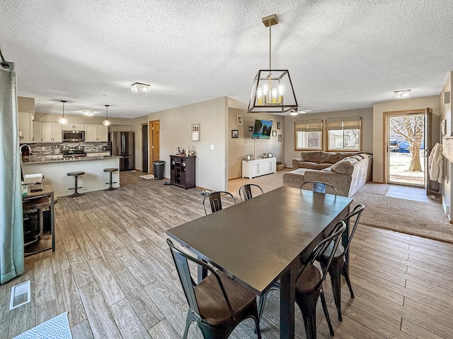 dining space featuring light wood-type flooring, visible vents, and a textured ceiling