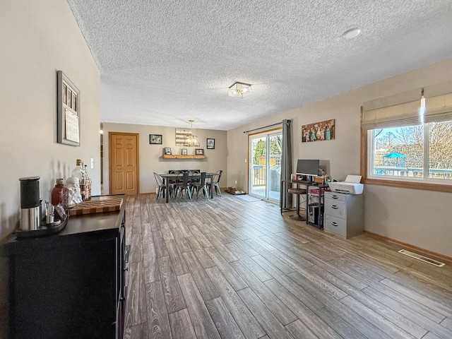 interior space with a textured ceiling, wood finished floors, visible vents, and baseboards