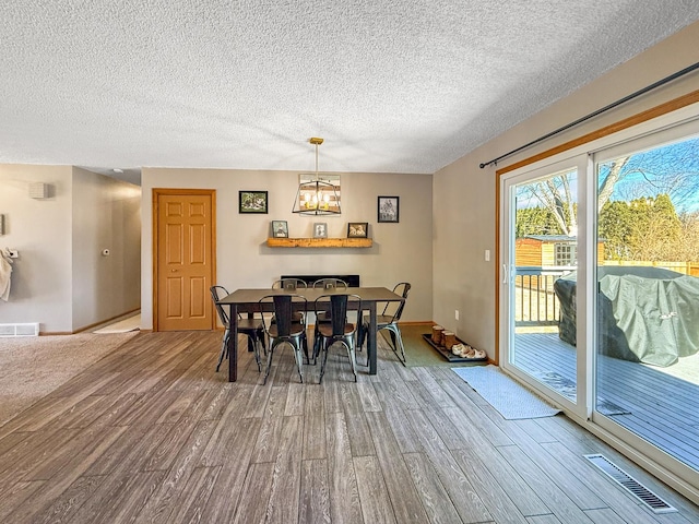 dining area with wood finished floors, visible vents, and an inviting chandelier