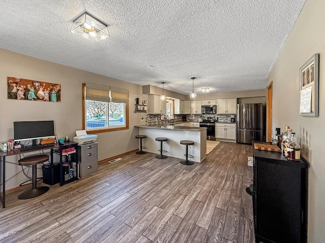 kitchen with stainless steel appliances, tasteful backsplash, wood finished floors, a peninsula, and a kitchen bar