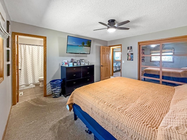 carpeted bedroom with a textured ceiling, ensuite bath, and a ceiling fan