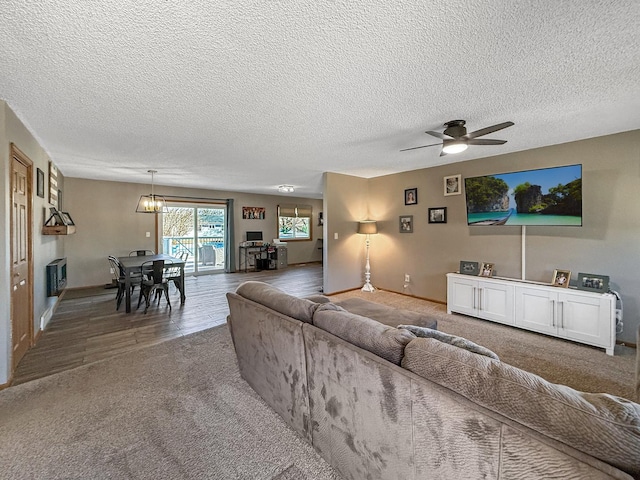 carpeted living room featuring ceiling fan with notable chandelier, a textured ceiling, and baseboards