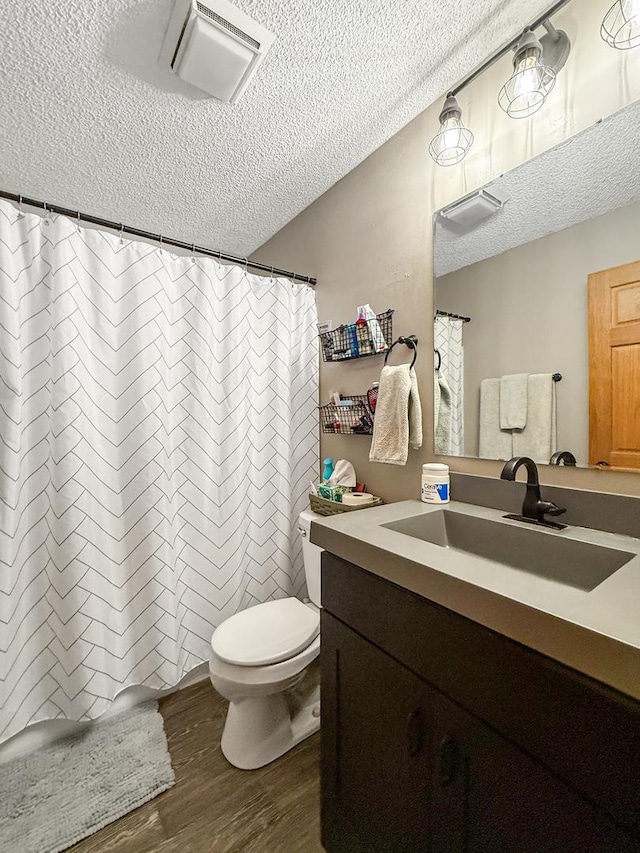 full bath featuring a textured ceiling, toilet, wood finished floors, vanity, and visible vents