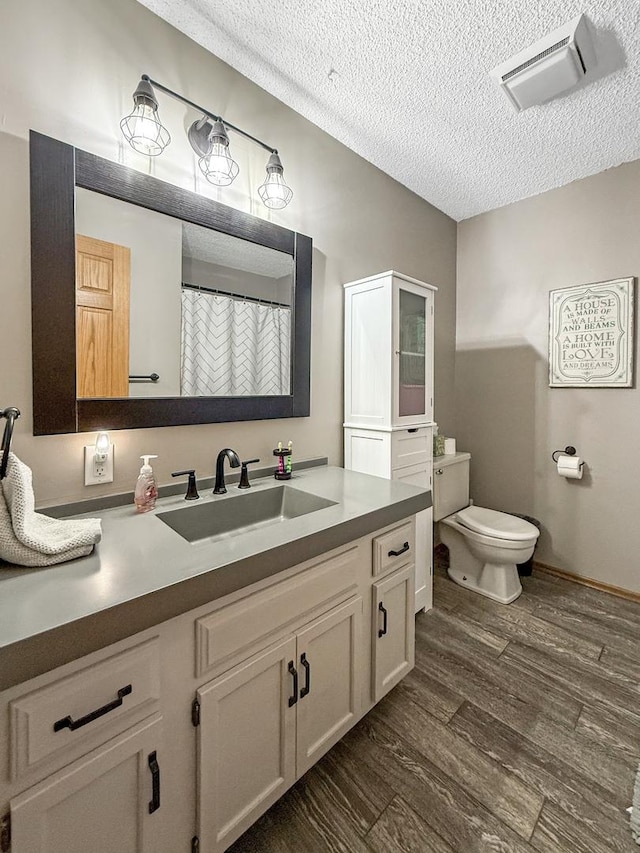 bathroom with visible vents, toilet, vanity, a textured ceiling, and wood finished floors