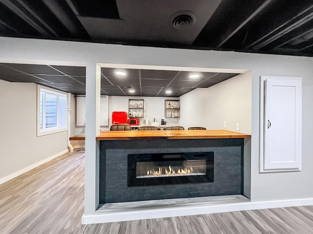 details with visible vents, a glass covered fireplace, wood finished floors, a drop ceiling, and baseboards