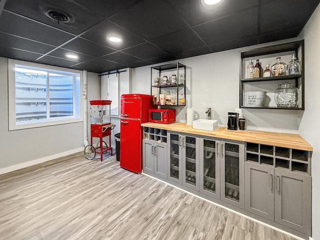 bar with white microwave, a drop ceiling, wood finished floors, and baseboards