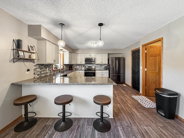 kitchen with stone countertops, tasteful backsplash, dark wood-type flooring, a peninsula, and stainless steel appliances