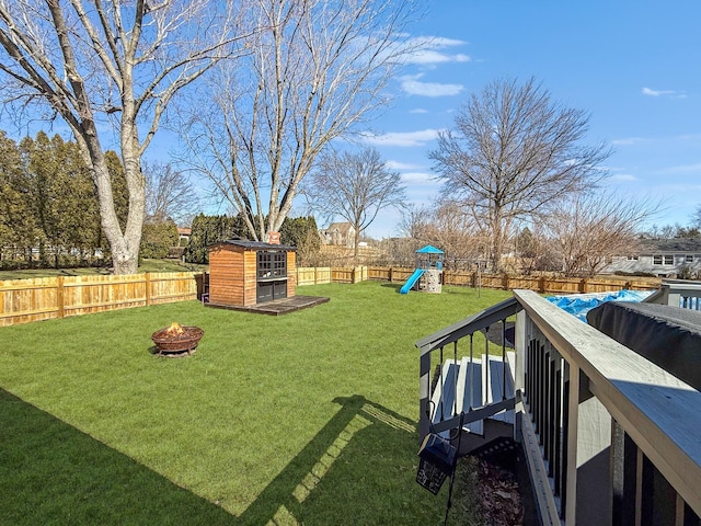 view of yard with a fire pit, a playground, a fenced backyard, and an outdoor structure