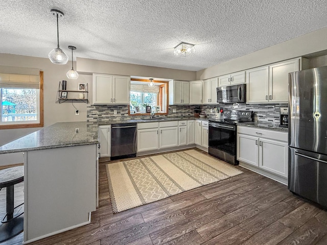 kitchen featuring appliances with stainless steel finishes, dark wood-type flooring, a peninsula, and decorative backsplash