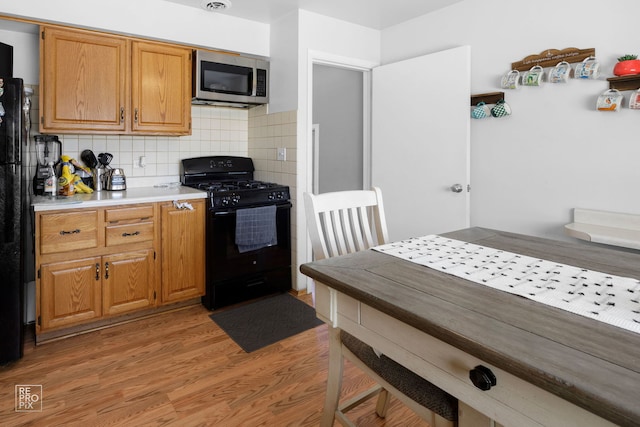 kitchen with light countertops, black appliances, light wood finished floors, brown cabinetry, and tasteful backsplash