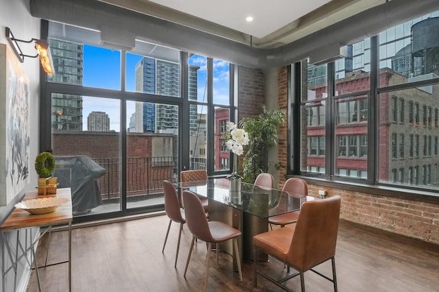 dining area with expansive windows, a city view, brick wall, and wood finished floors