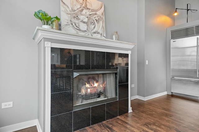 interior details featuring baseboards, stainless steel built in fridge, a tiled fireplace, and wood finished floors