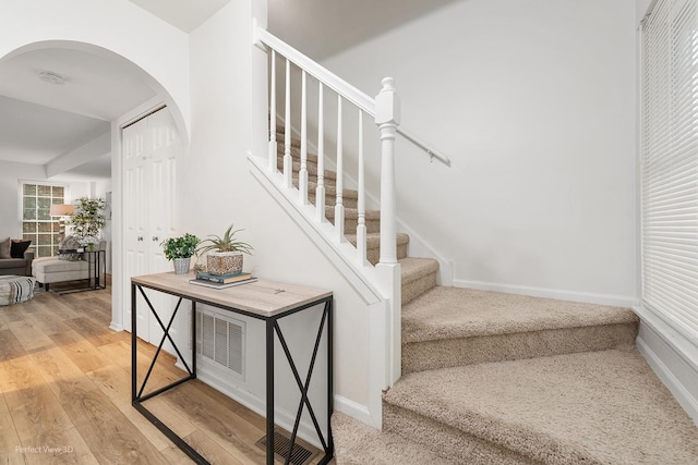 stairs with baseboards, visible vents, arched walkways, and wood finished floors