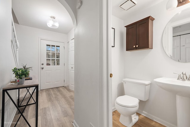 half bath featuring visible vents, baseboards, toilet, wood finished floors, and a sink