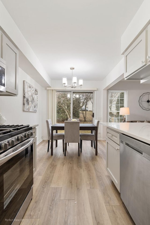 kitchen with light wood-style flooring, a notable chandelier, stainless steel appliances, hanging light fixtures, and light countertops