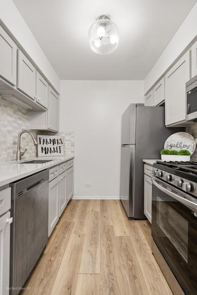 kitchen featuring tasteful backsplash, light countertops, appliances with stainless steel finishes, a sink, and light wood-type flooring