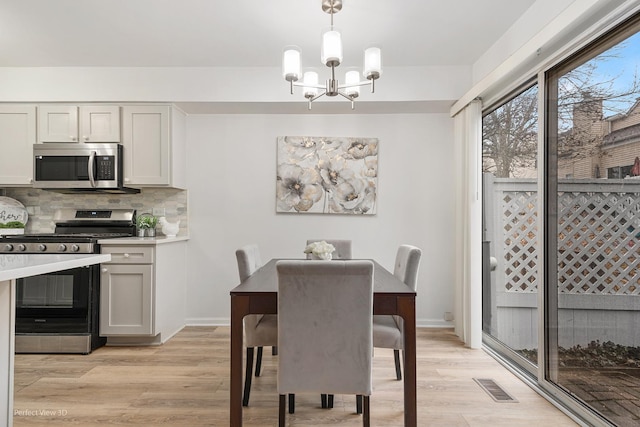 dining space with light wood-style floors, visible vents, a notable chandelier, and baseboards