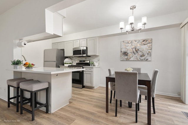 kitchen with decorative backsplash, appliances with stainless steel finishes, light wood-type flooring, a kitchen bar, and a chandelier