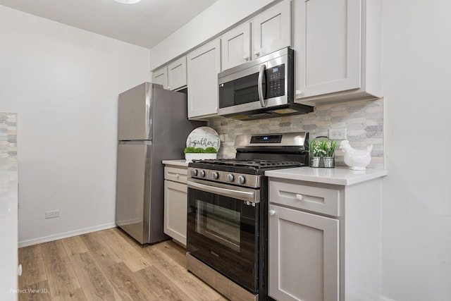 kitchen featuring tasteful backsplash, light countertops, appliances with stainless steel finishes, light wood-type flooring, and baseboards