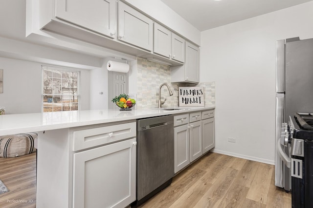 kitchen with stainless steel appliances, decorative backsplash, a sink, light wood-type flooring, and a peninsula