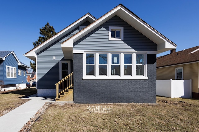 bungalow featuring entry steps, brick siding, fence, and a front yard