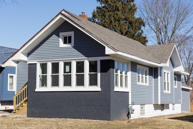 view of side of home featuring roof with shingles, brick siding, and a chimney