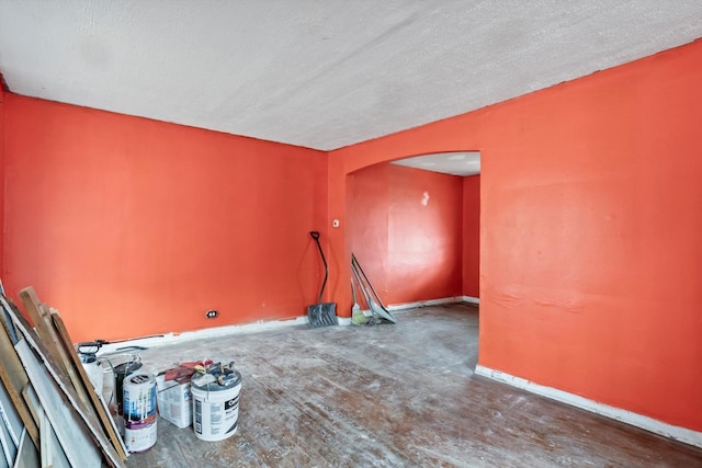 unfurnished room with arched walkways, a textured ceiling, and baseboards