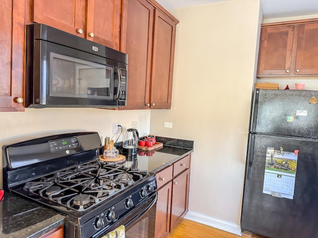 kitchen featuring black appliances, baseboards, light wood finished floors, and dark stone countertops