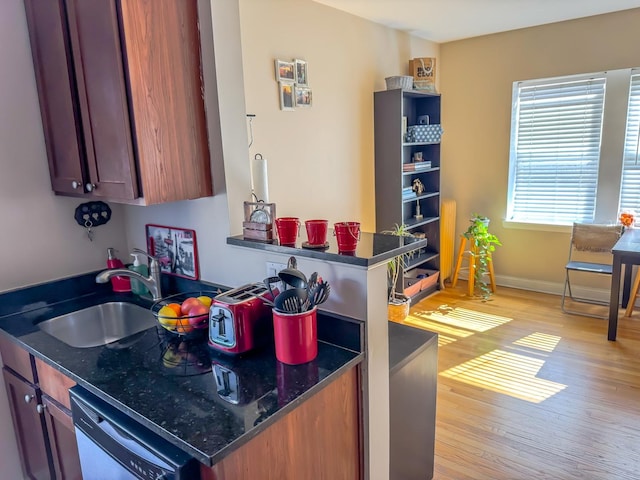 kitchen with baseboards, dark stone counters, dishwasher, light wood-style floors, and a sink