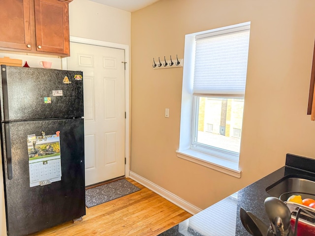 kitchen featuring baseboards, freestanding refrigerator, light wood finished floors, brown cabinetry, and dark countertops