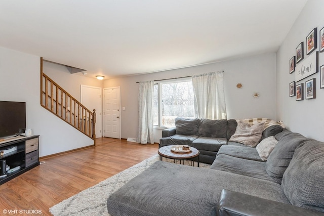 living room featuring stairs, baseboards, and light wood finished floors