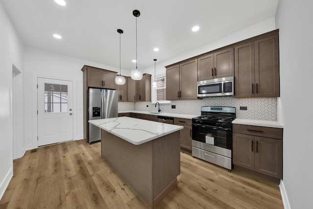 kitchen featuring light wood finished floors, backsplash, appliances with stainless steel finishes, a sink, and a kitchen island