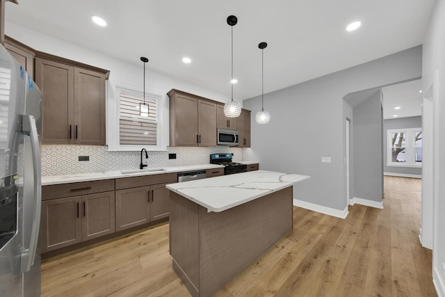 kitchen featuring a center island, stainless steel appliances, backsplash, a sink, and light wood-type flooring